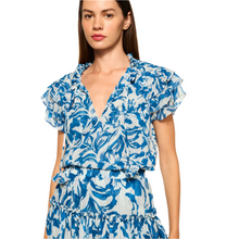 Load image into Gallery viewer, The Maria top is made from blue and white watercolor chiffon, featuring an easy silhouette with short, tiered ruffle sleeves and a ruffle-trimmed split neckline with petal tassel ties. The body is self-lined, and the top can be paired with the coordinating Marion skirt for a seamless daytime look. Made in the USA, it is crafted from 100% Poly Chiffon and recommended for dry cleaning.
