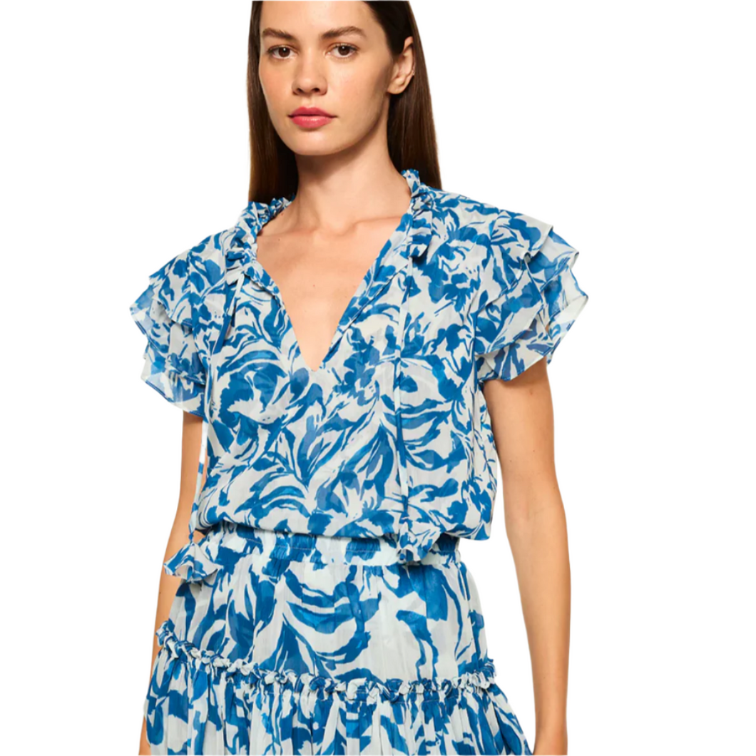 The Maria top is made from blue and white watercolor chiffon, featuring an easy silhouette with short, tiered ruffle sleeves and a ruffle-trimmed split neckline with petal tassel ties. The body is self-lined, and the top can be paired with the coordinating Marion skirt for a seamless daytime look. Made in the USA, it is crafted from 100% Poly Chiffon and recommended for dry cleaning.