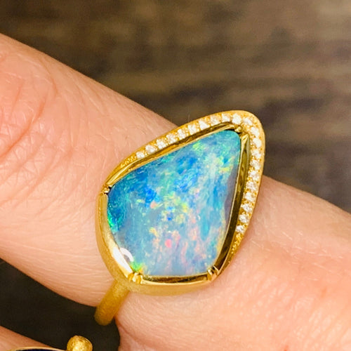 Nestled at the heart of this exquisite creation is a boulder opal of unparalleled beauty. Its captivating play-of-color dances across the surface, revealing an intricate spectrum of iridescence reminiscent of a hidden oasis within the opal's depths. The opal's rich hues, ranging from deep ocean blues to fiery oranges and lush greens, create an ever-shifting kaleidoscope of enchantment that holds the gaze and ignites the imagination. 18K YG   Opal 6.38ct, Diamond pave .21c